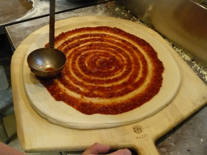 Abo's proprietary Rocky Graziano sauce being hand-spread on fresh dough